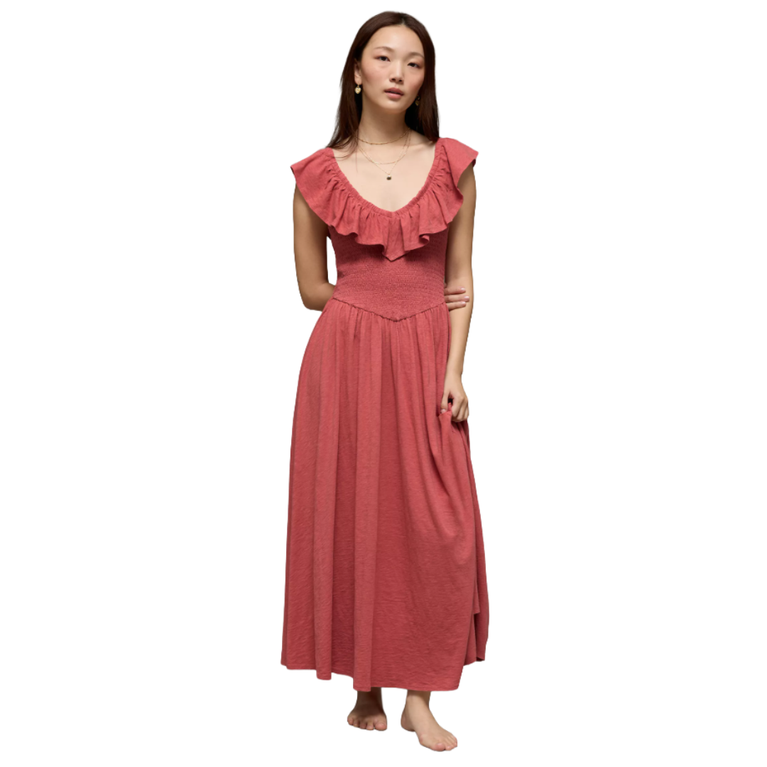A woman in a sleeveless, ruffled, pink maxi dress with a fitted bodice and flowing skirt, accessorized with earrings and necklaces.