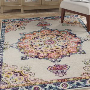 An ornate area rug with a central medallion design in vibrant colors including pink, orange, and blue, set against a light background. It's partially under a piece of furniture on a wooden floor.
