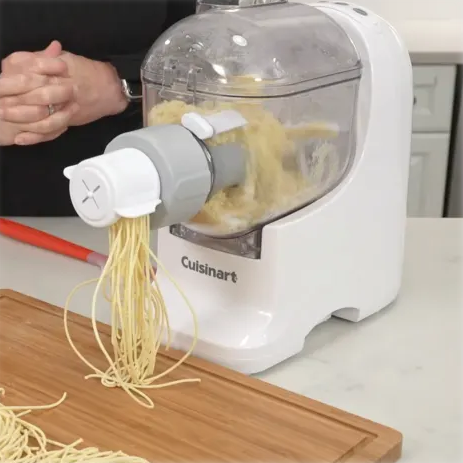 Cuisinart pasta maker extruding fresh spaghetti onto a wooden cutting board.