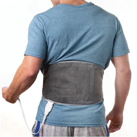 A person wears a gray heating pad around their lower back, secured with a strap and connected to a control cord.