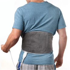 A person wears a gray heating pad around their lower back, secured with a strap and connected to a control cord.