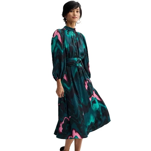 A woman is wearing a Nine West Midi Dress featuring a teal, pink, and black abstract pattern. The dress has long puff sleeves, a high neckline, and a belted waist, creating an elegant silhouette.