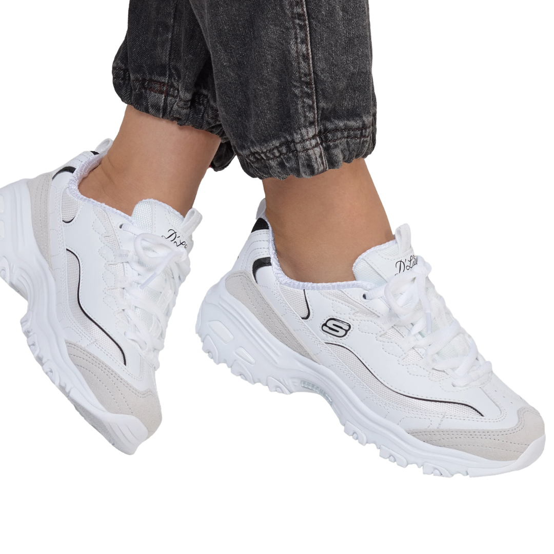 A person wearing white Skechers D'Lites sneakers with black detailing and light beige accents, paired with rolled-up dark jeans.