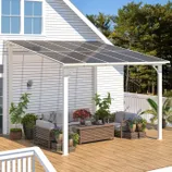 A patio awning with a pergola design and transparent panels provides shade for outdoor furniture, surrounded by potted plants on a wooden deck.