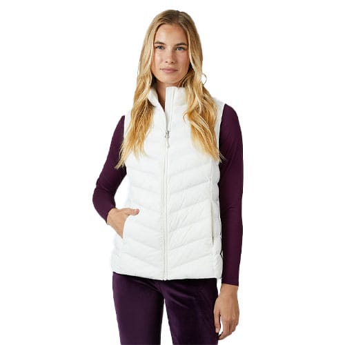 A woman wearing a white quilted vest over a long-sleeve dark purple top, with her hand in the vest pocket.