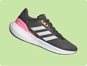 Gray athletic shoe with white stripes, pink heel accent, and orange eyelet on a light green background.