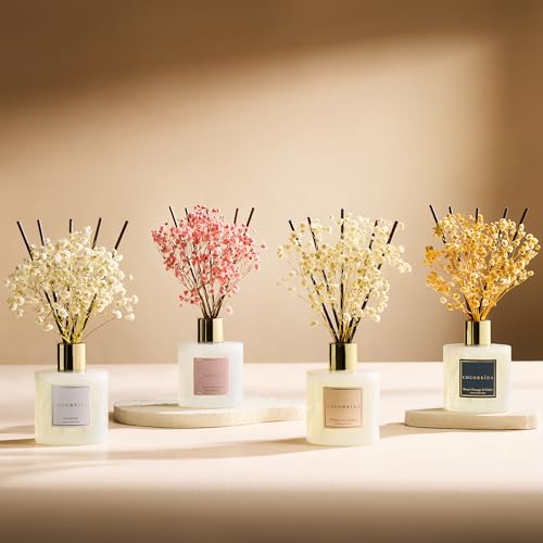 Four diffusers with dried flower arrangements and reed sticks in white containers, each labeled with a different fragrance name: \“Fresh Cut Flowers,\“ \“Magnolia & Peony,\“ \“Ginger & White Tea,\“ and \“Coconut & Calm.\“