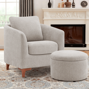 Light gray upholstered armchair with a curved design, accompanied by a matching round ottoman. The setup is in a cozy room featuring a patterned rug, curtains, and an ornate fireplace with decorative items.