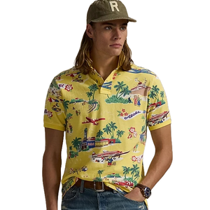 A man wears a yellow polo shirt with a tropical print featuring airplanes, palm trees, and retro cars, paired with jeans and a cap with an \“R\“ on it.