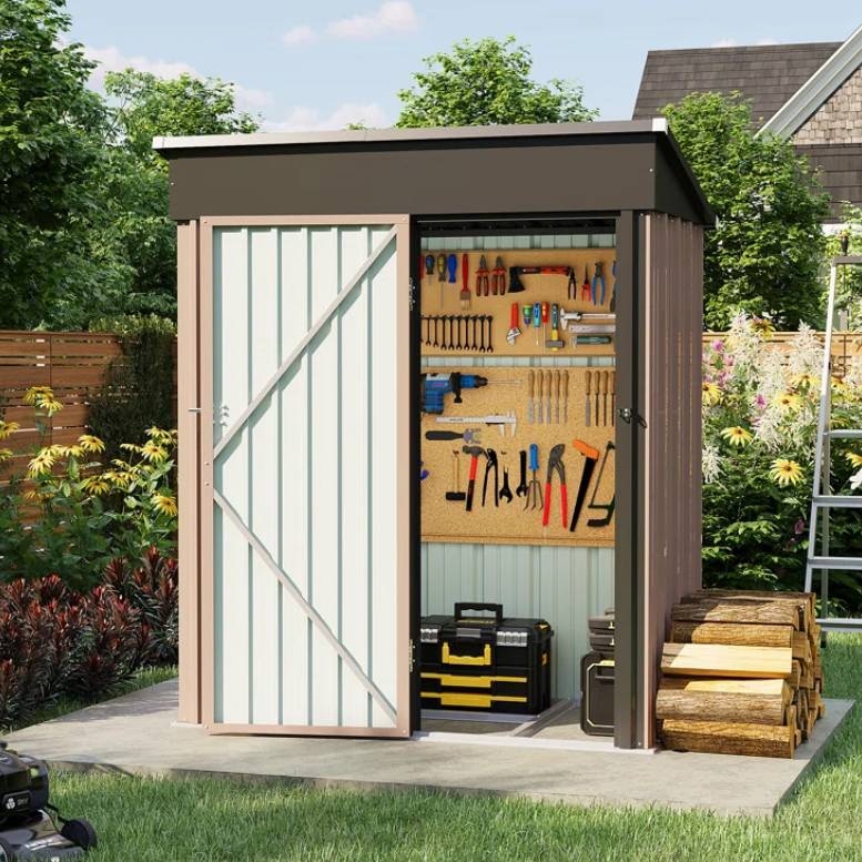 A small metal storage shed with a sliding door, featuring a tool organizer on the interior wall with various hand tools and power tools. Firewood is stacked outside on a concrete slab, surrounded by a garden with flowers and trees.