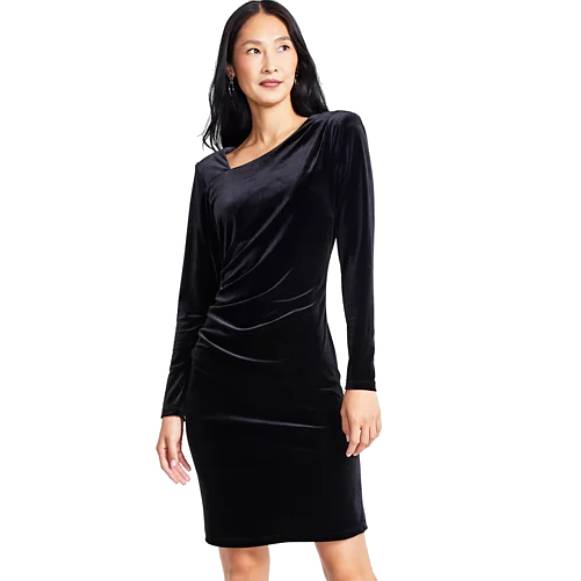 A woman is wearing a black long-sleeve velvet dress with a draped design. The dress is knee-length and has a fitted silhouette.