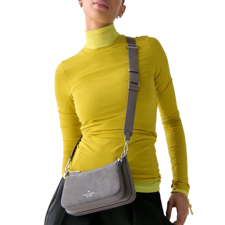 Person wearing a yellow turtleneck and black skirt with a gray Kate Spade New York crossbody bag featuring an adjustable strap.