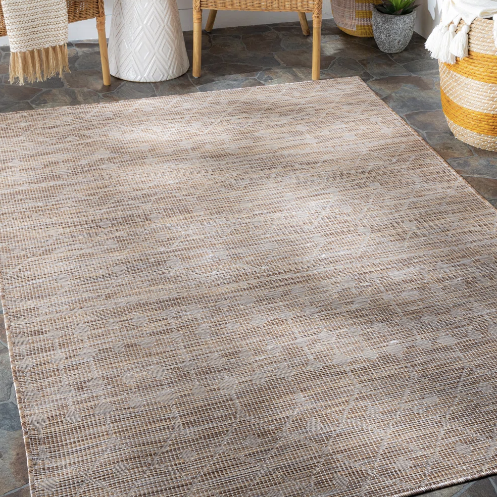 A textured beige area rug with a subtle geometric pattern on a stone tile floor, accompanied by wicker furniture and decorative baskets.