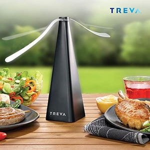 A black Treva bug repeller fan with soft, flexible blades is shown on a table during an outdoor meal, designed to keep insects away from the food.