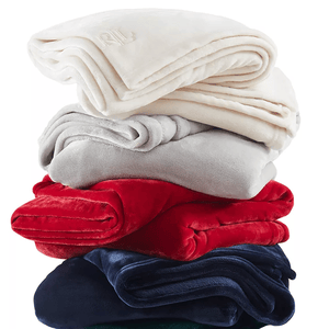 A stack of folded soft blankets in different colors: cream, gray, red, navy, and green.