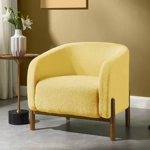 A cozy yellow armchair with wooden legs is next to a small side table holding a white vase with flowers and accompanied by a black and gold floor lamp. The setting is in a modern, warmly lit room with an abstract painting on the wall.