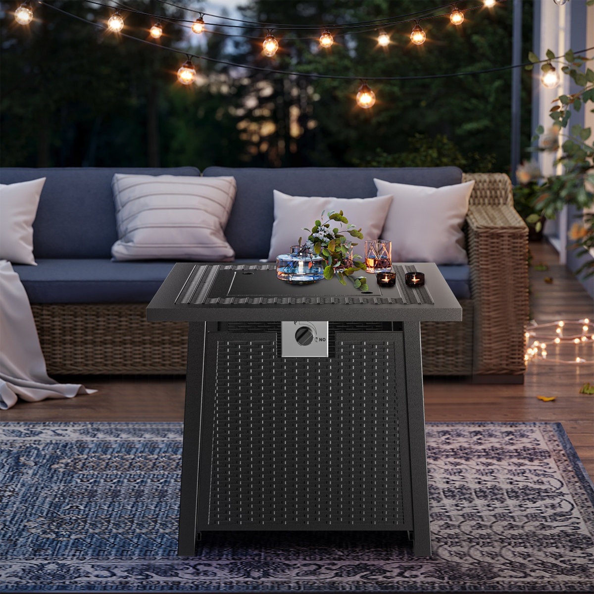 A stylish outdoor patio scene with a wicker-style fire pit table adorned with candles and a flower arrangement; string lights and a wicker sofa with cushions create a cozy ambiance.