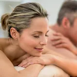 A couple is enjoying a relaxing massage in a spa setting with lit candles around them.