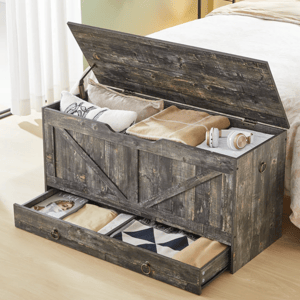A rustic wooden storage bench with an open lid reveals blankets, pillows, and headphones, while a lower drawer stores additional items including a magazine.