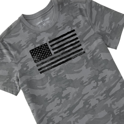 A camouflage-patterned gray T-shirt with a distressed American flag graphic on the chest, branded with \“Life is Good.\“