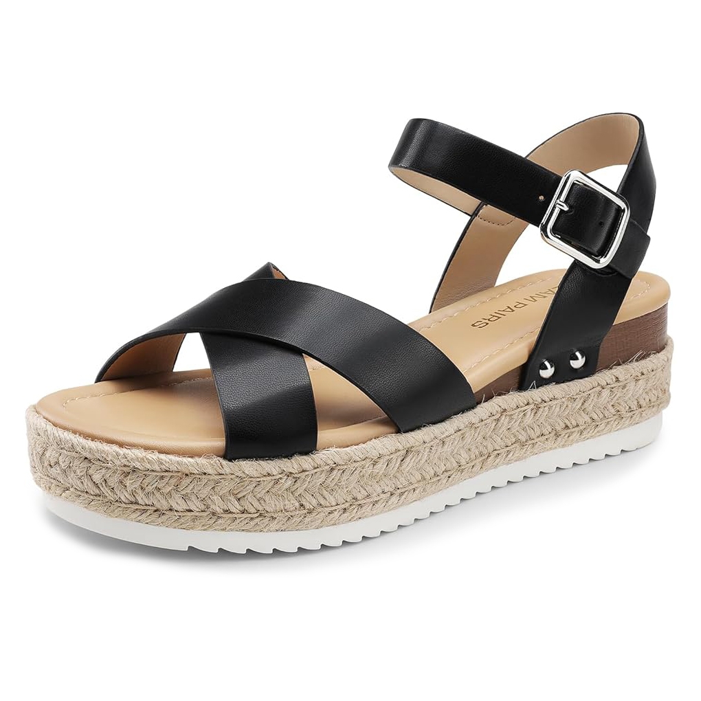 Black leather espadrille wedge sandals with a braided jute platform, featuring cross-over straps and an adjustable ankle strap with a silver buckle. The sole is white with a slight grip for added stability.