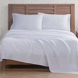 A bed is adorned with matching white sheet sets featuring a geometric diamond pattern, paired with two pillowcases on a wooden headboard.