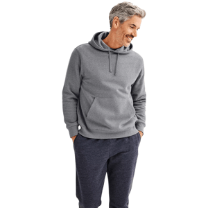 A man is wearing a gray hooded sweatshirt with a front pocket and navy sweatpants. He's standing with his hands in the pockets, smiling, against a plain background.