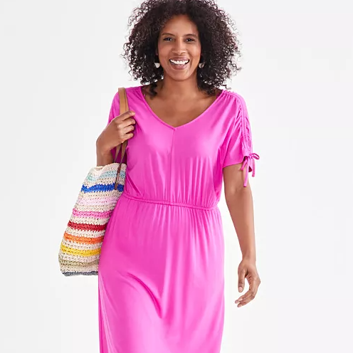 A vibrant pink midi dress with ruched sleeves and a drawstring tie at the waist, accompanied by a multicolored striped tote bag.