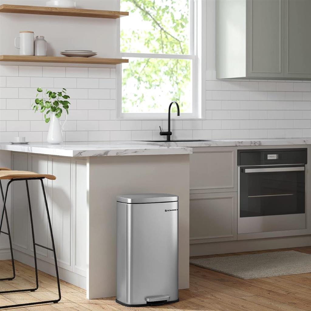A modern kitchen with stainless steel trash can, white cabinetry, floating shelves, and built-in appliances.