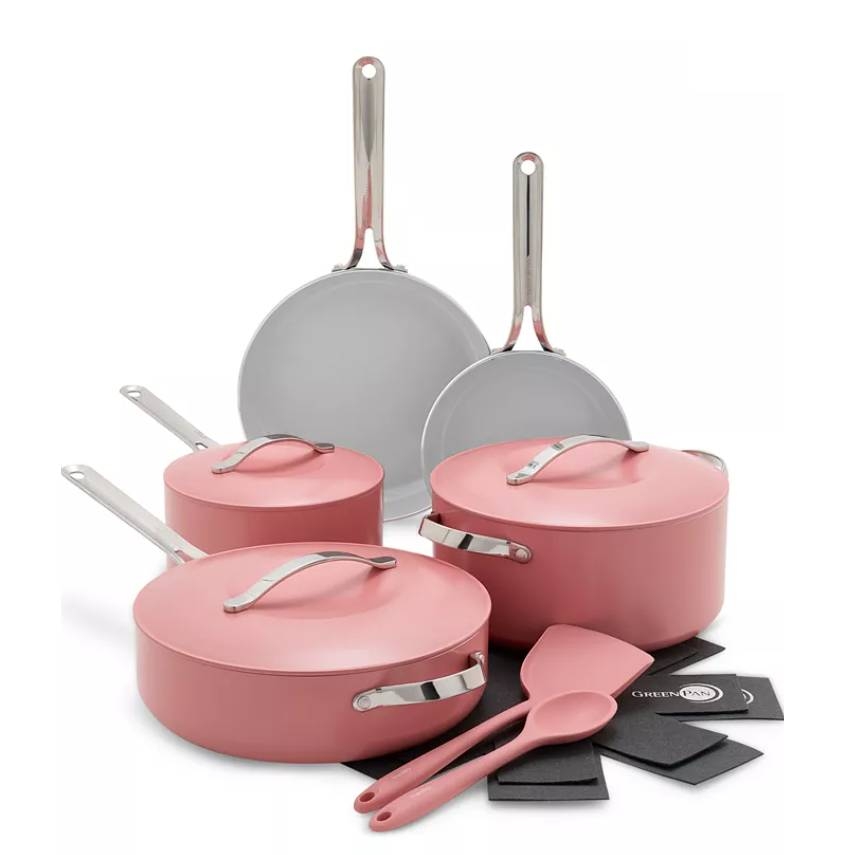 A pink cookware set featuring a variety of pots, pans, and lids, accompanied by matching utensils and protective pads. Handles are metallic.