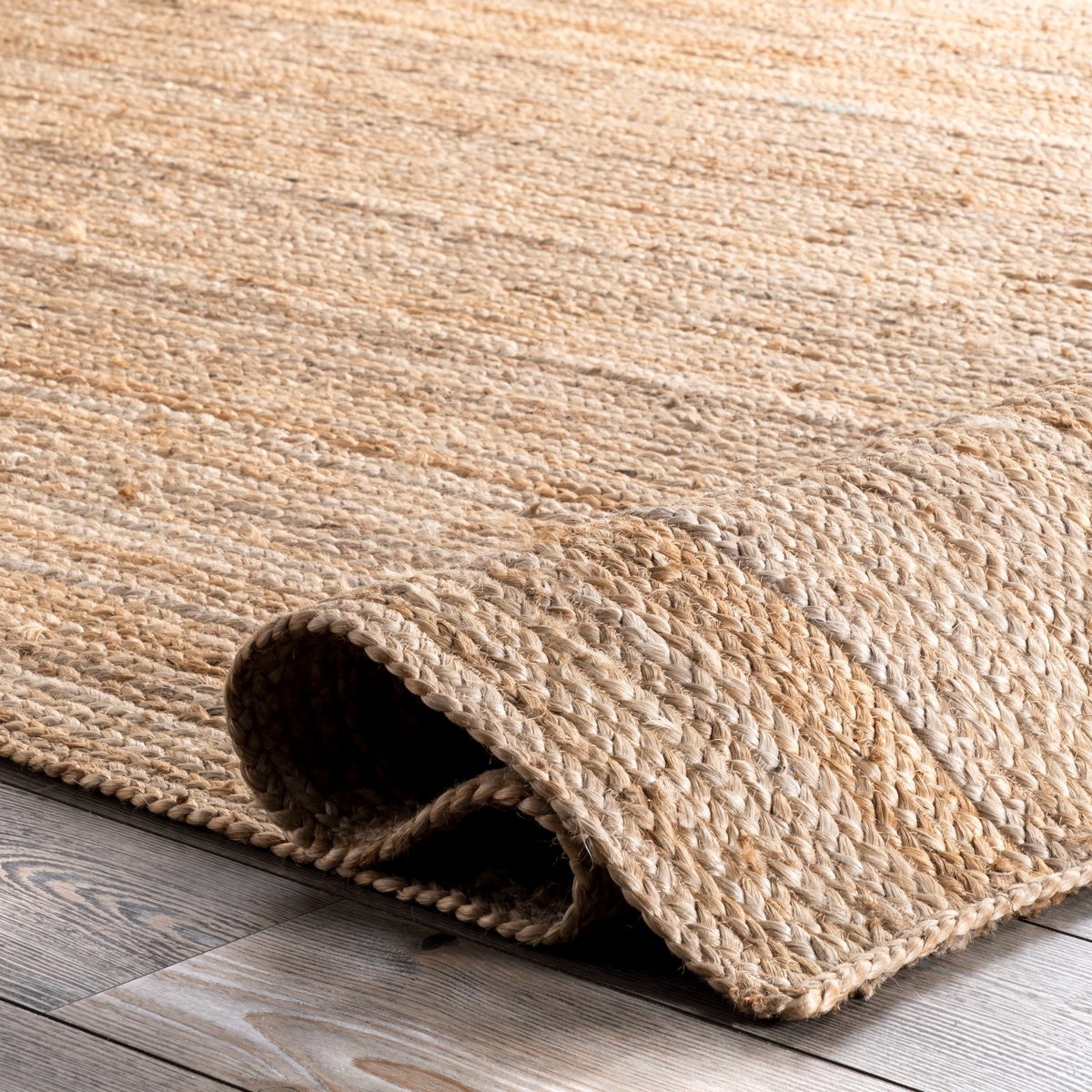 A natural woven jute rug is partially rolled on a light wooden floor, showcasing its textured design.