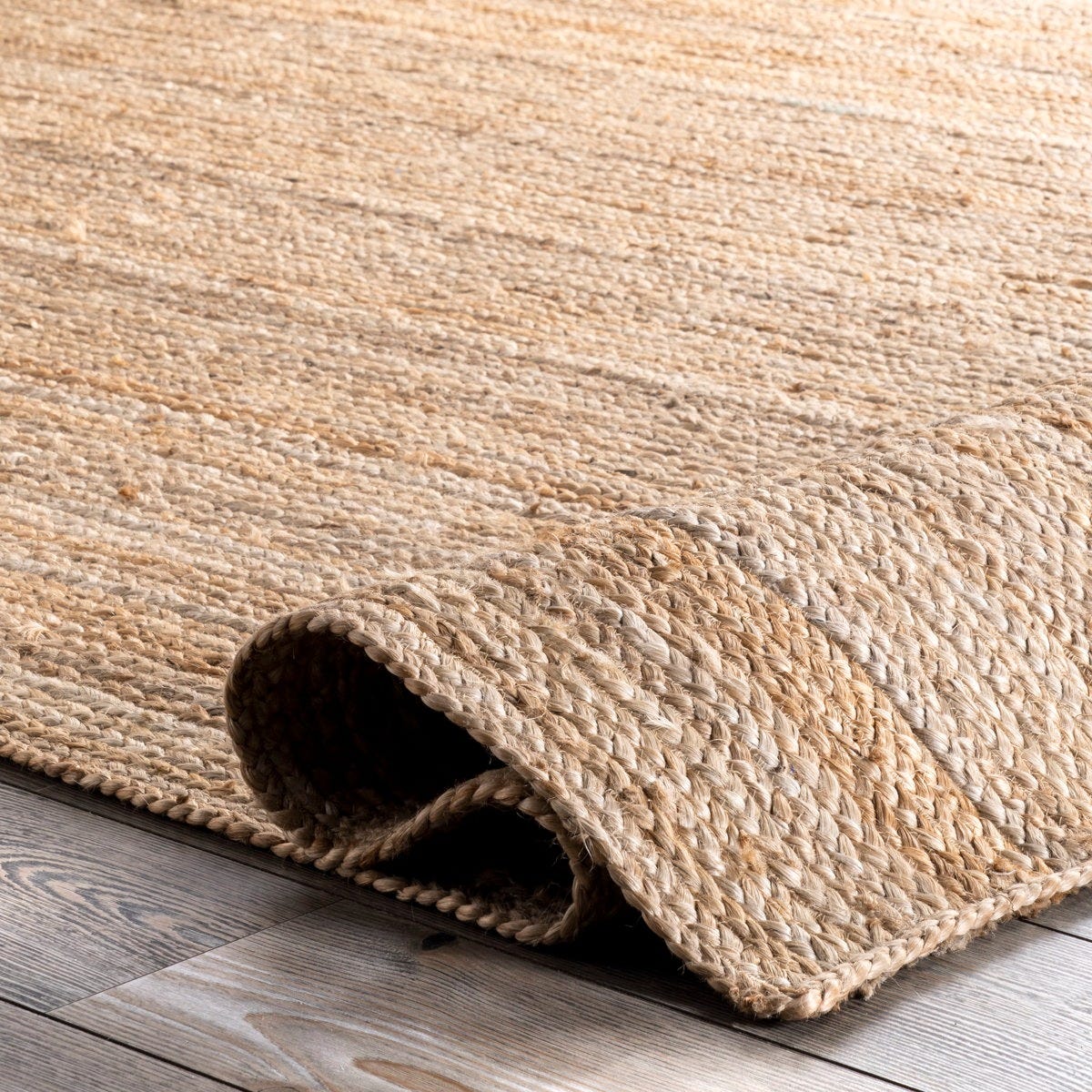 A natural woven jute rug is partially rolled on a light wooden floor, showcasing its textured design.