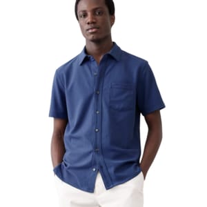 Blue short-sleeve shirt with a button-up front, single chest pocket, and a soft, honeycomb-textured pique fabric. Worn with white pants.