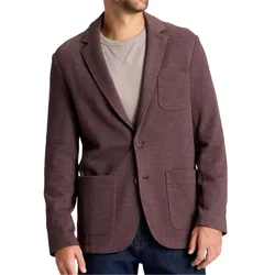 A man is wearing a maroon two-button blazer with patch pockets, layered over a grey textured sweater, paired with dark jeans.