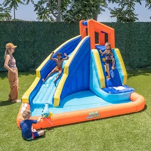 An inflatable water slide with climbing wall and splash pool, featuring children playing on it and an adult supervising.