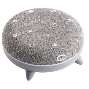 A round device with a fabric top featuring touch-control icons, resting on short legs, serves as a sound machine and night light.