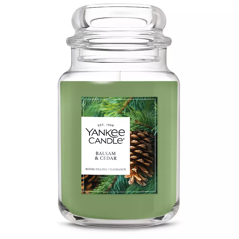 Yankee Candle in Balsam & Cedar scent, featuring a green wax in a large jar. Fragrance is described as room-filling, with imagery of pine cones and evergreen branches.