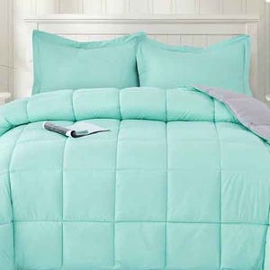A light turquoise comforter set with two matching pillow shams on a bed, featuring a quilted design. A book is placed on the comforter.