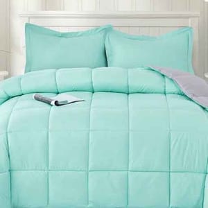 A light turquoise comforter set with two matching pillow shams on a bed, featuring a quilted design. A book is placed on the comforter.
