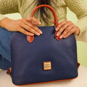 A navy blue Dooney & Bourke pebble leather domed satchel with brown leather handles and accents, featuring a gold-tone logo plate on the front.