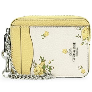 Yellow and white leather card holder with floral prints, featuring a silver chain and Coach branding.