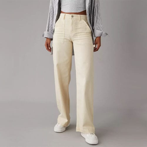 A person is wearing high-waisted, wide-leg pants in a light cream color, paired with a cropped shirt and white sneakers.