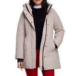 A woman is wearing a light beige winter coat with a hood, over a black sweater and white shirt. She pairs it with red pants.