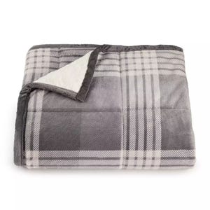 A gray plaid blanket with a sherpa lining is shown, folded with the corner turned up to reveal its soft interior.