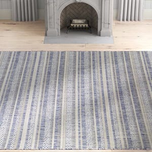 A striped rug featuring blue and beige tones is placed on a light wooden floor in front of a decorative gray fireplace.