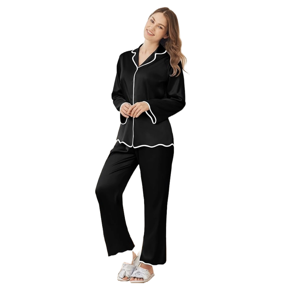 Women's satin pajamas in black with white piping, featuring a long-sleeve button-up top and matching pants. The outfit is completed with open-toe sandals adorned with bows.