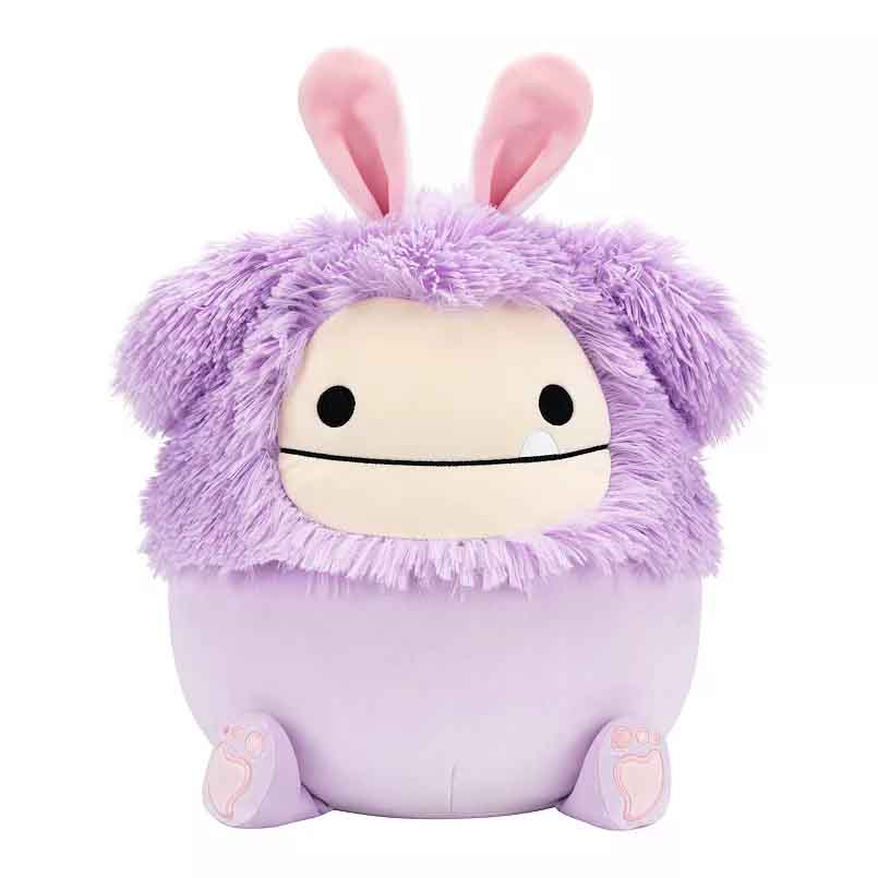 A plush Squishmallows character with a round shape, lavender body, fuzzy purple fur, floppy ears, and simple black eyes. It has soft features and resembles a playful, cute creature.