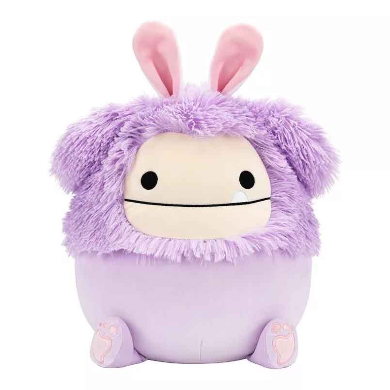 A plush Squishmallows character with a round shape, lavender body, fuzzy purple fur, floppy ears, and simple black eyes. It has soft features and resembles a playful, cute creature.