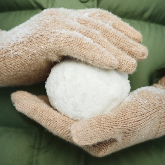 A person wearing beige gloves holds a snowball against a green background.