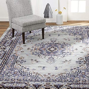 A traditional-style area rug featuring a central medallion pattern with floral motifs in shades of gray, blue, and beige, bordered by navy and tan accents.